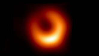 An image of a supermassive black hole in galaxy M87, taken by the Event Horizon Telescope. The image shows an orange-gold ring around the black hole with the brightest spot appearing toward the bottom right of the ring in this image.