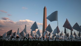 A sea of white flags planted in the ground wave in front of the Washington Memorial. Each flag represented a person in the United States who had died from COVID-19 by early fall 2021.