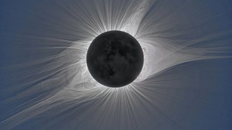 White tendrils in the solar corona frame a heavily shadowed moon during a solar eclipse